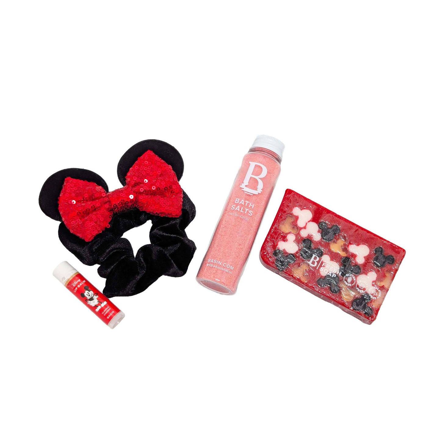 Licensed Basin Disney spa essentials set featuring a pink bath salts bottle, Mickey Mouse cherry lip balm, red Mickey silhouette bar soap, and a Minnie Mouse inspired black scrunchie hair tie with red sequined ears for custom Orlando resort gift boxes