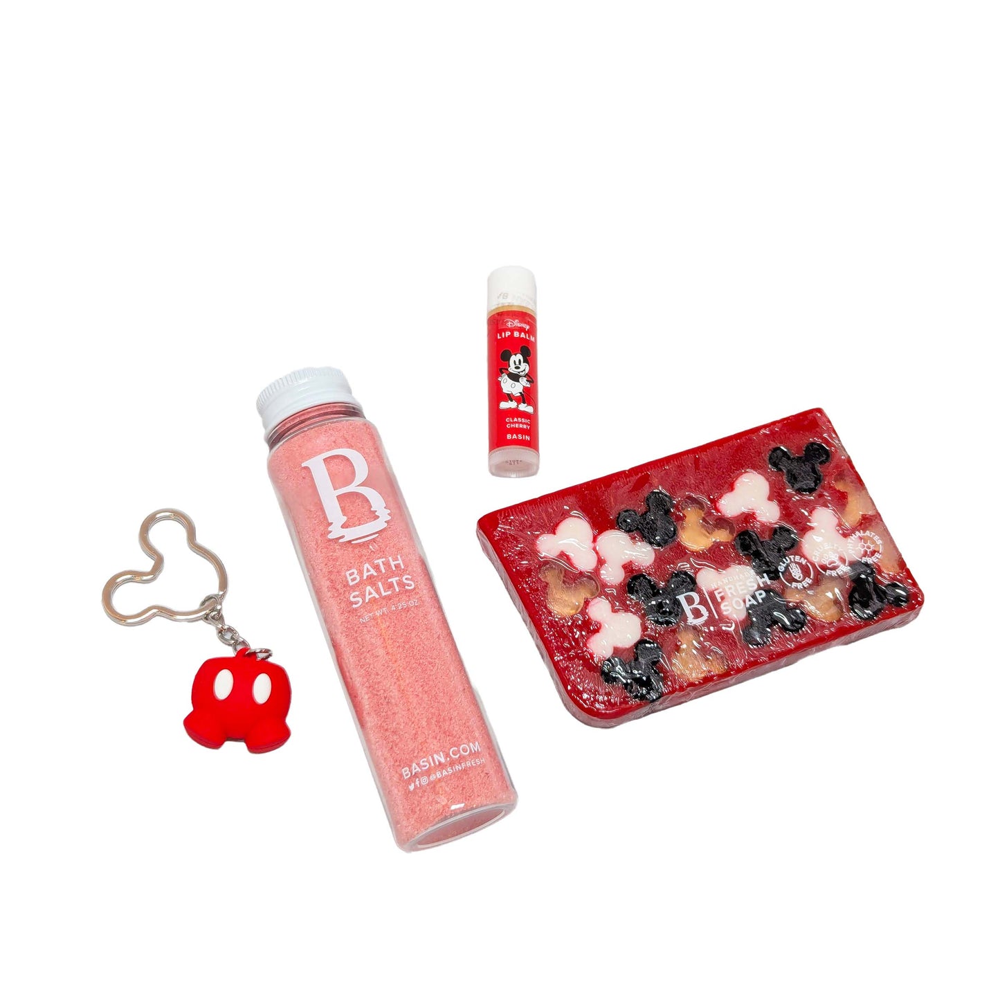 Licensed Basin Disney spa essentials set featuring a pink bath salts bottle, Mickey Mouse cherry lip balm, red Mickey silhouette bar soap, and a Mickey Mouse shaped red pants keychain for custom Orlando resort gift boxes