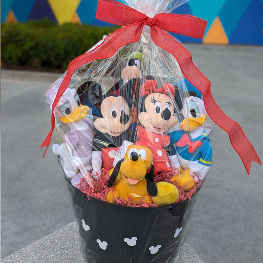 A gift basket containing plush toys of Mickey Mouse, Minnie Mouse, Goofy, Donald Duck, and Pluto, tied together with a red ribbon, perfect for Walt Disney World resort deliveries
