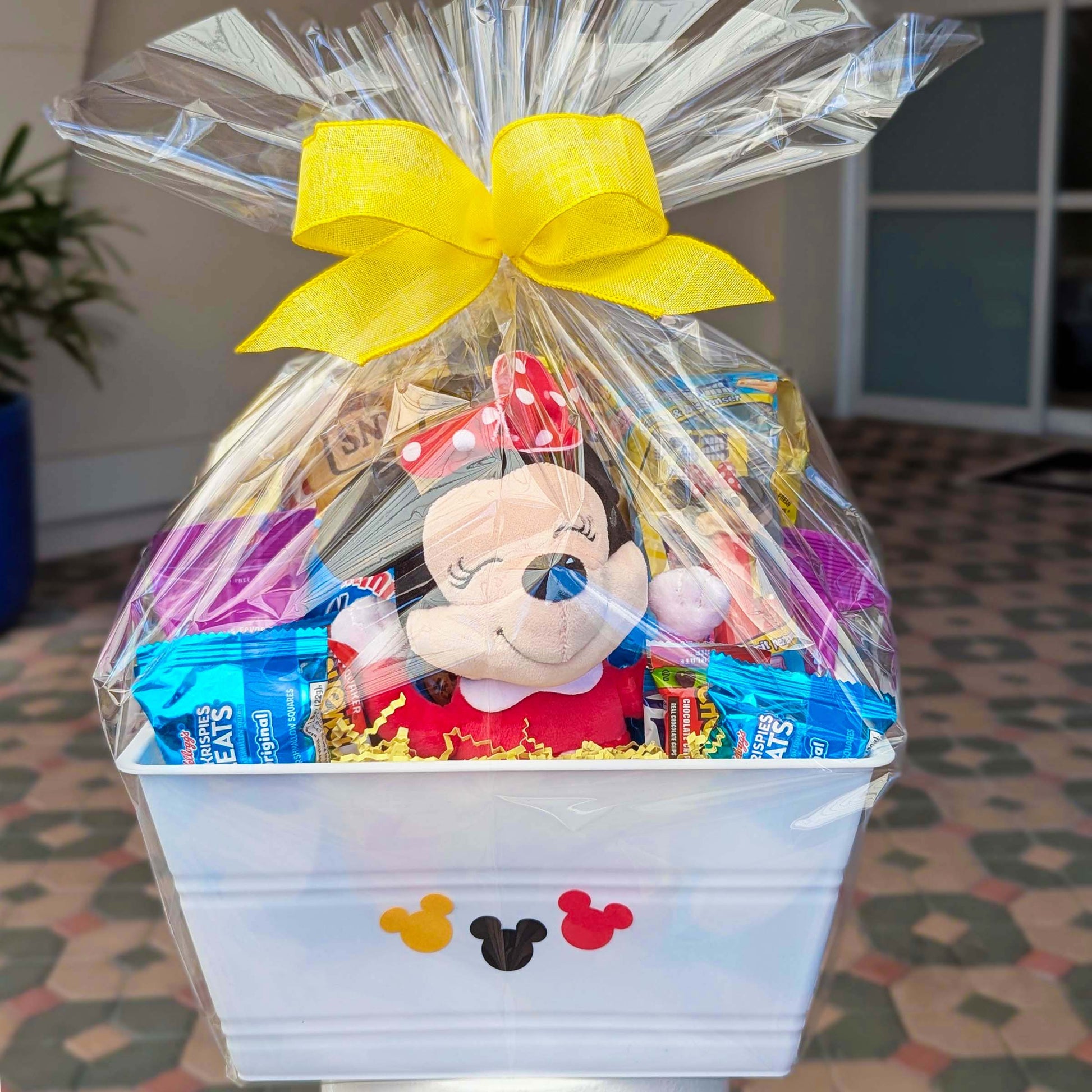 Custom Disney Minnie Mouse gift basket filled with a licensed 8-inch plush toy and assorted snacks with a yellow bow for Orlando resort delivery