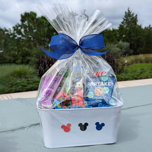 Disney themed snack gift basket in a white crate with Mickey Mouse silhouettes, wrapped in cellophane with a blue bow for Orlando resort delivery