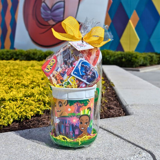 Disney-themed gift basket containing a refillable popcorn bucket, snacks, and a PEZ dispenser, tied together with a yellow ribbon for Orlando resort delivery