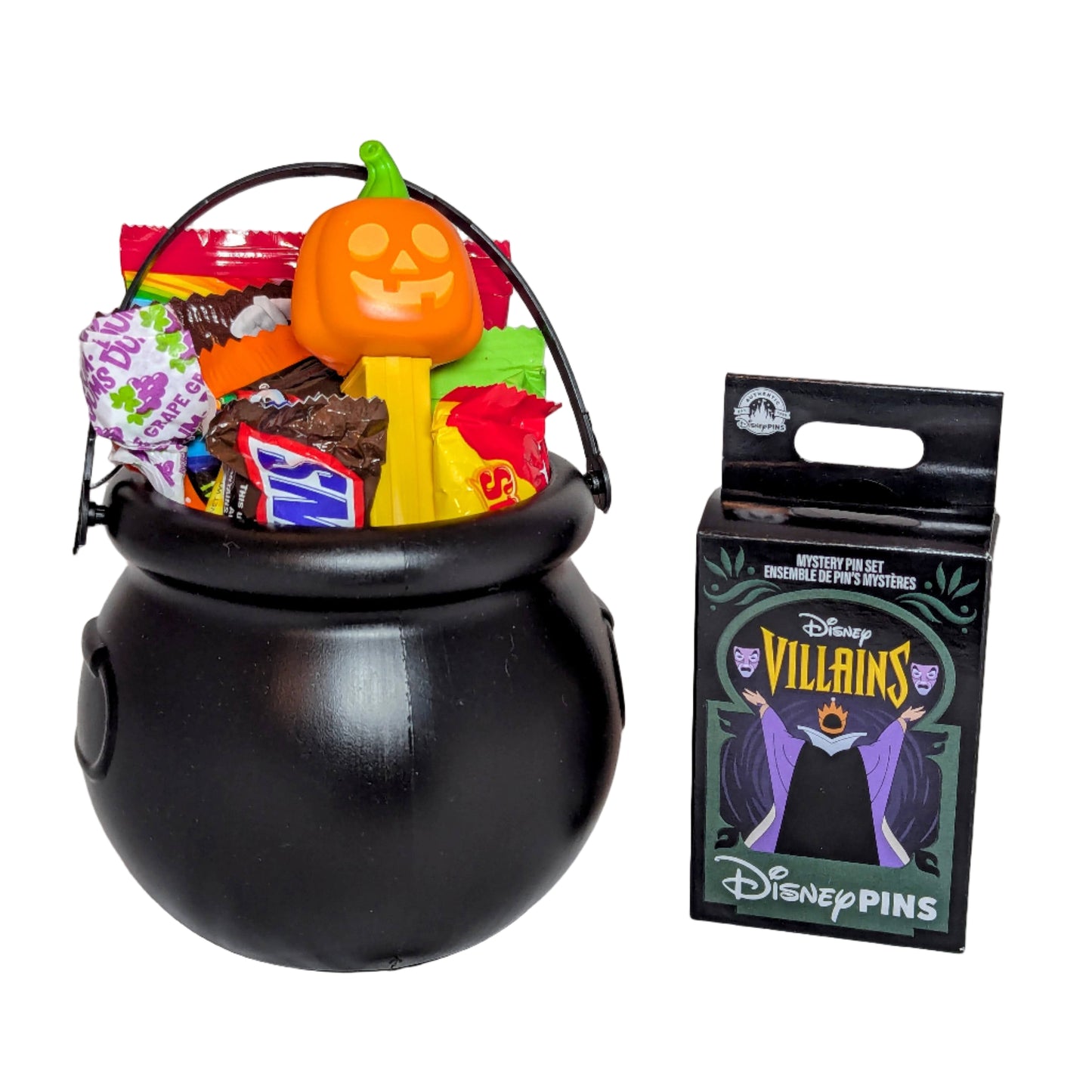 Mini Halloween black cauldron bucket filled with sweet treats and a pumpkin PEZ dispenser next to a Disney Villains mystery pin box