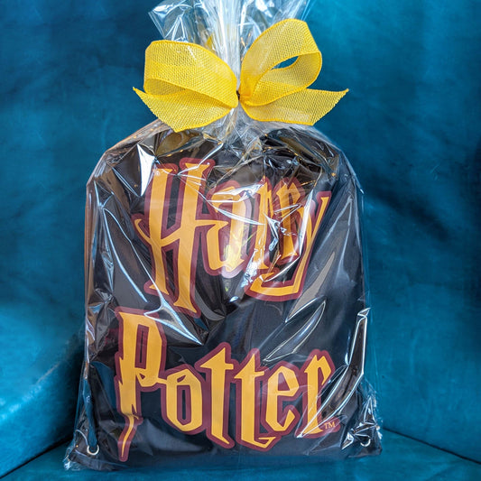 Harry Potter themed gift basket featuring a licensed drawstring backpack and assorted snacks wrapped in clear cellophane with a yellow bow for Universal Orlando resort hotel delivery