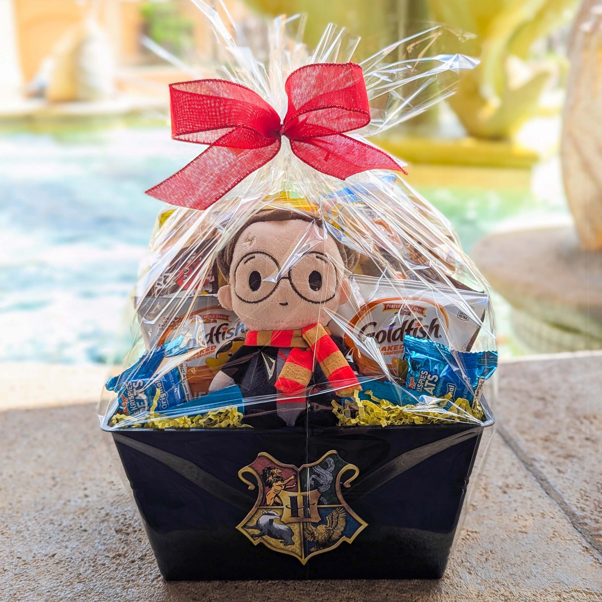 Harry Potter themed gift basket featuring a licensed bean bag plush toy and assorted snacks wrapped in clear cellophane with a red bow for Universal Orlando resort delivery
