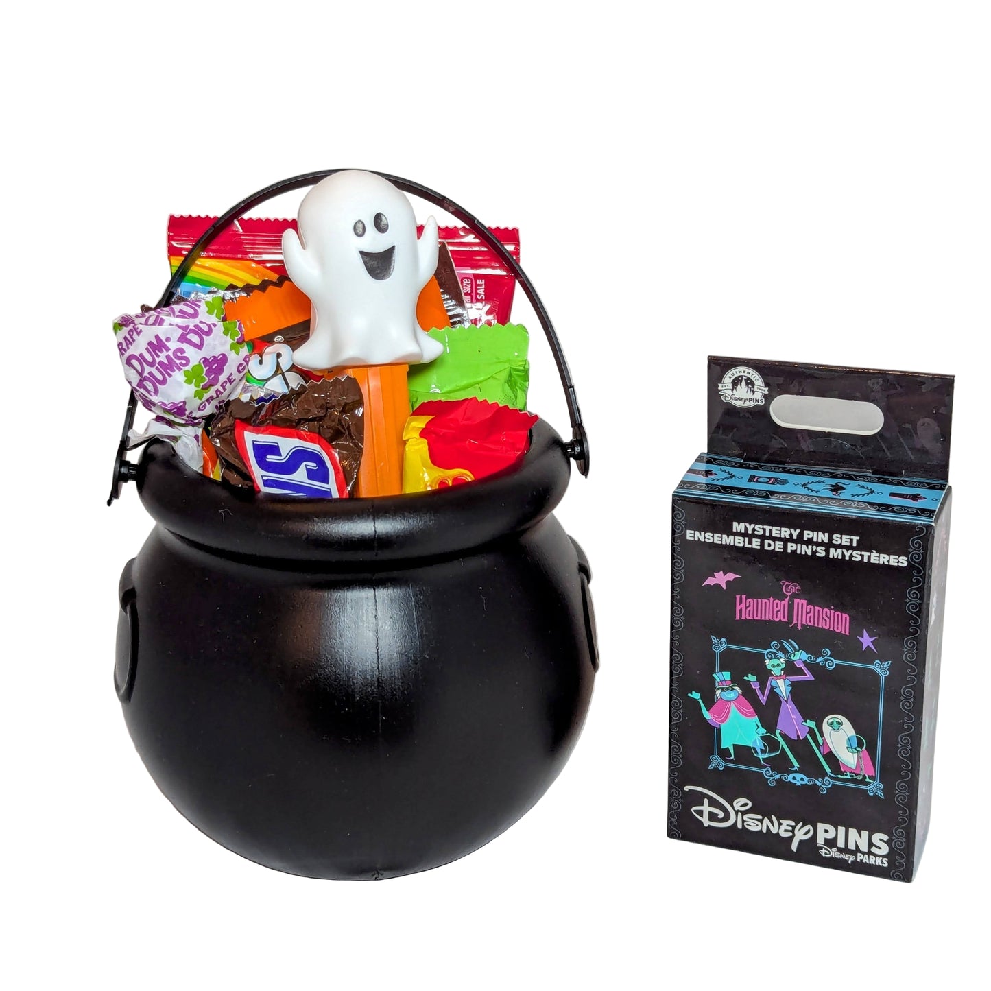 Mini Halloween black cauldron bucket filled with sweet treats and a ghost PEZ dispenser next to a Disney Haunted Mansion mystery pin box