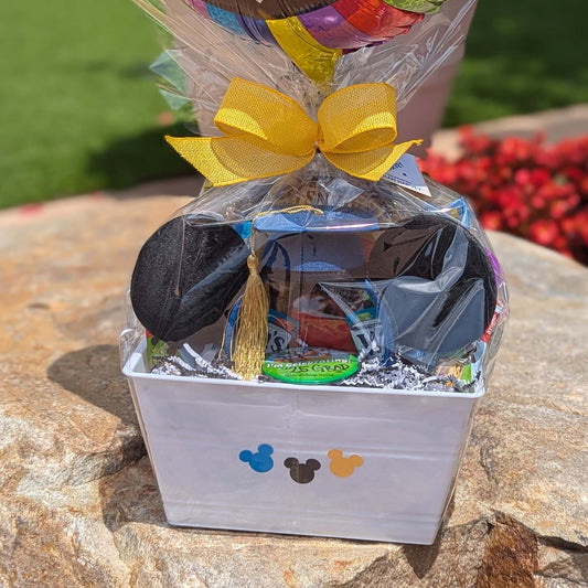 Mickey Mouse graduation themed gift basket in a white crate wrapped in clear cellophane with a large yellow bow for Disney resort delivery