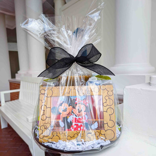 Mickey Mouse wooden photo frame and snack gift basket wrapped in clear cellophane with a decorative black mesh bow