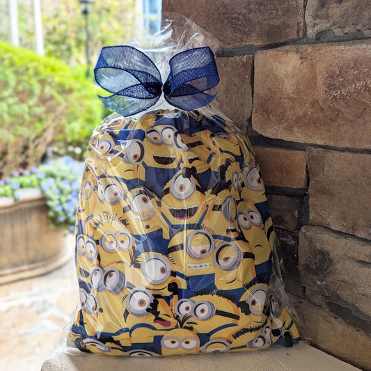Minions themed gift basket featuring a licensed drawstring backpack and assorted snacks wrapped in clear cellophane with a blue bow for Universal Orlando resort hotel delivery