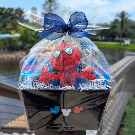 Spider-Man themed plush and snack gift basket in a black crate with Mickey Mouse silhouettes, wrapped in clear cellophane with a blue bow for Orlando resort delivery